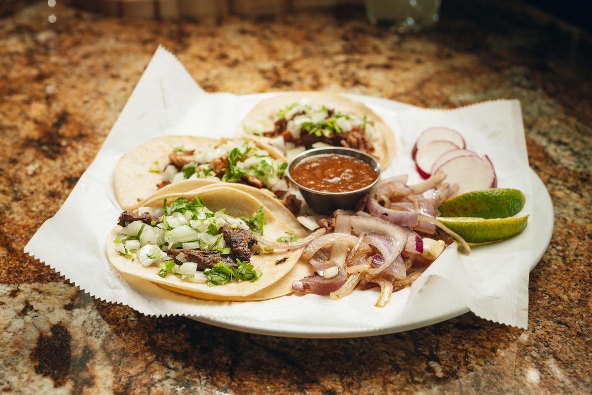 Three street tacos with cilantro, onion, radish, lime, and salsa